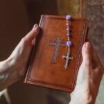 Dłonie trzymające biblie na której leży różaniec