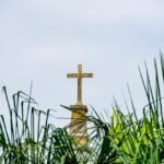 Betonowy krzyż stojący na tle niebieskiego nieba w otoczeniu roślin