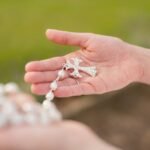 Biały różaniec z krzyżem trzymany w rękach kobiety
