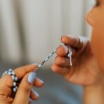 Kobieta trzymająca w rękach różaniec całuje krzyżyk