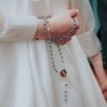 Kobieta stojąca obok męża trzymająca w ręku niebieski różaniec