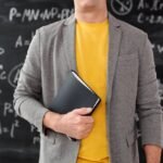 Nauczyciel trzymający teczkę w ręku a w tle tablica klasowa