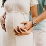 Kobieta w ciąży i jej mąż trzymający ją za brzuch