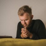 Mężczyzna modlący się przy łóżku z biblią