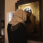 Kobieta w szaliku na głowie modląca się do obrazu Matki Bożej