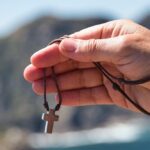 Dłoń mężczyzny trzymająca krzyżyk na sznurku