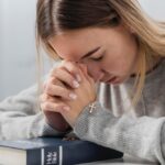 Młoda dziewczyna z biblią i krzyżem w ręce modląca się w intencji brata