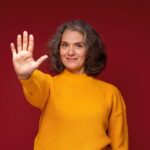Kobieta w żółtym swetrze pokazująca dłoniom liczbę pięć