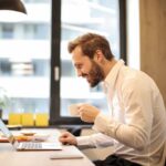 Mężczyzna pracujący w biurze pijący kawę przed komputerem