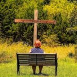 Kobieta siedząca na ławce modląca się przed krzyżem