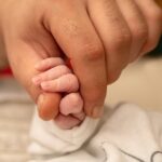Dłoń mężczyzny trzymająca rączkę małego dziecka, noworodka
