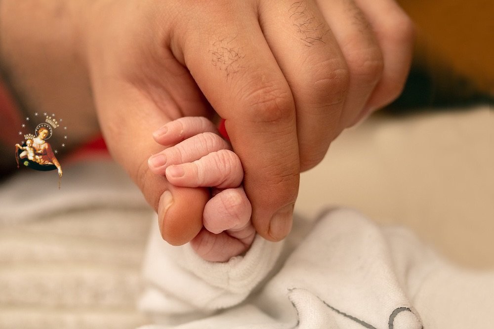 Dłoń mężczyzny trzymająca rączkę małego dziecka, noworodka